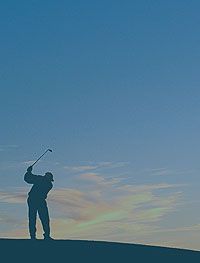 Silhouette of a golfer against a blue sky